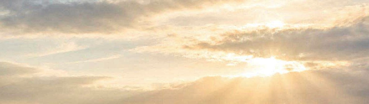 Golden light breaking through soft clouds in a peaceful sky.